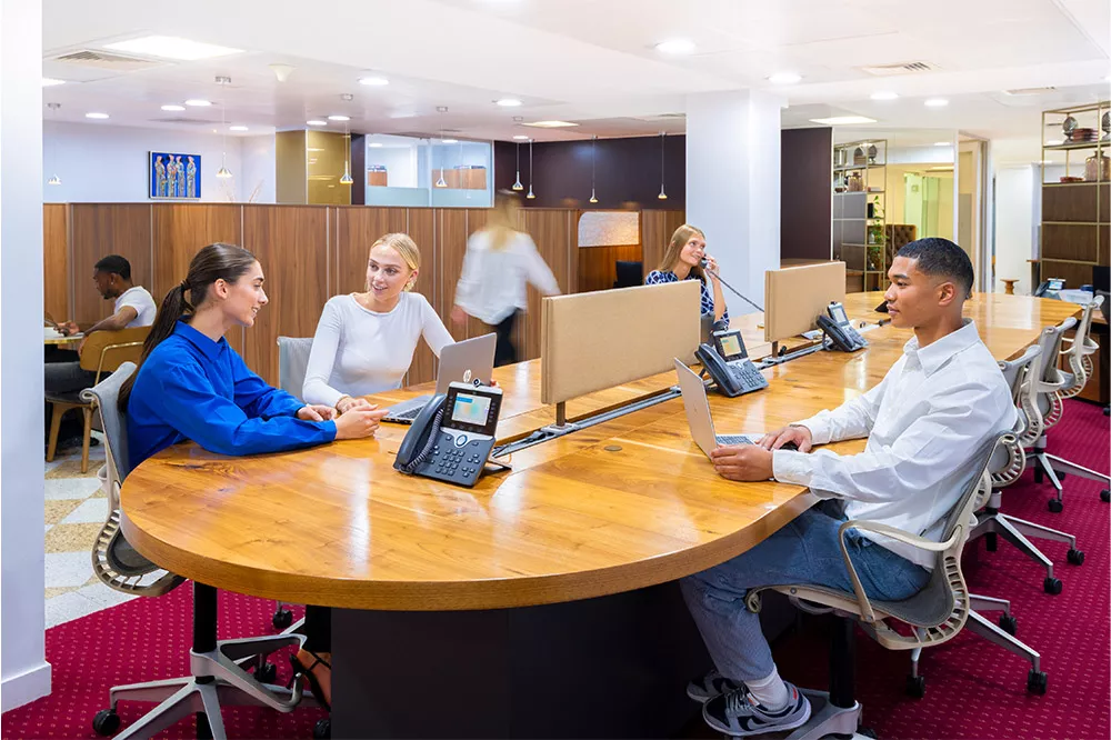 Client working and answering calls at Mayfair Coworking Space featuring a high shared desk and booths.